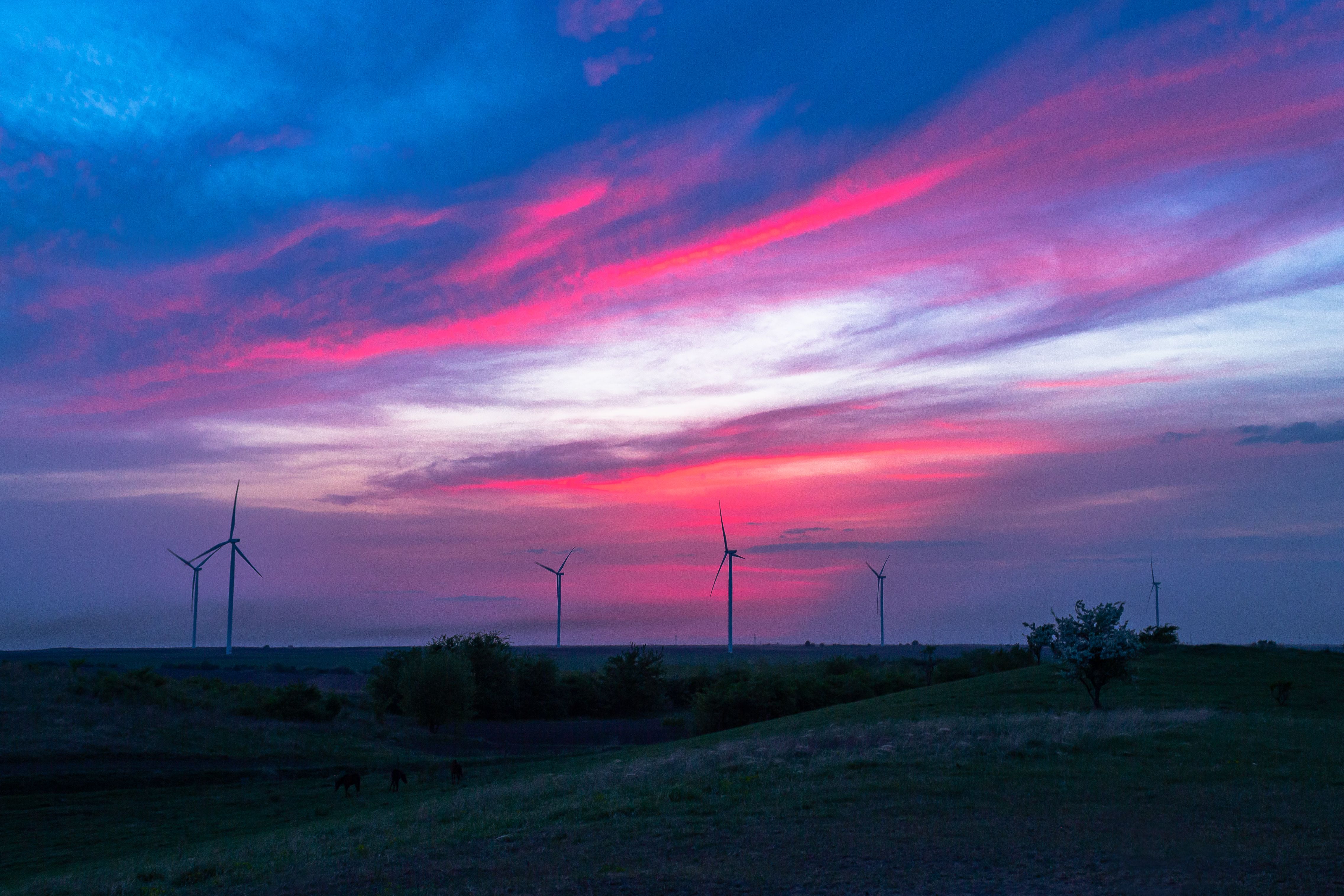 Wind turbines silhouetted against a vivid pink and blue sunset sky over open grassland